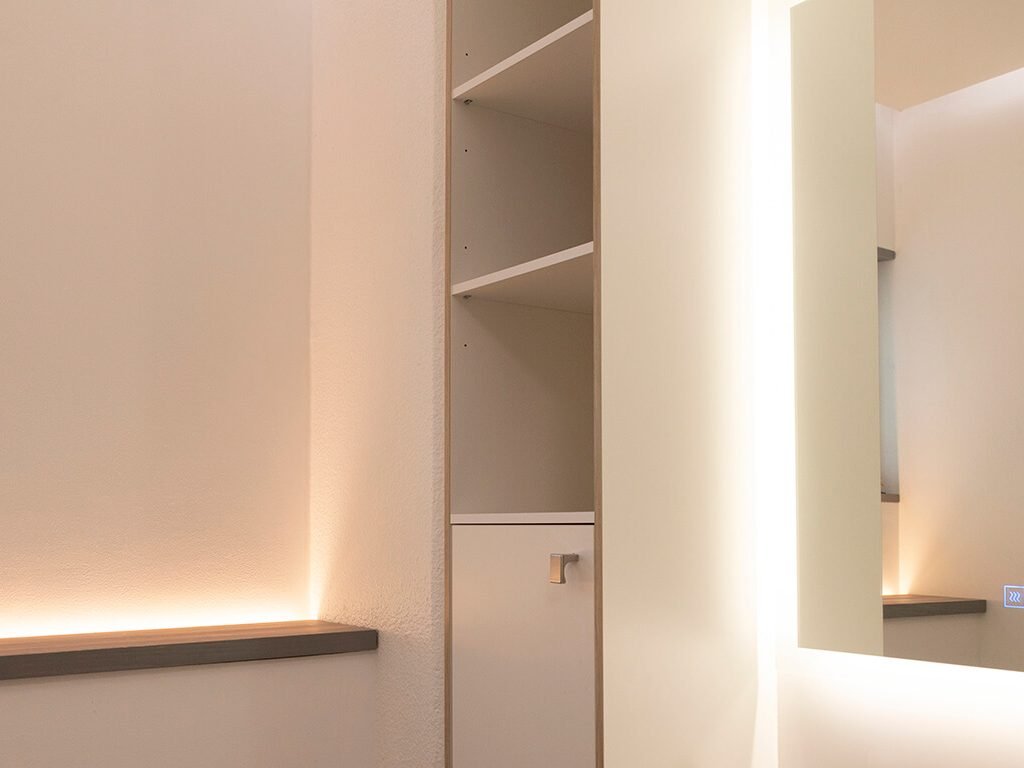Minimalistinen sisustus, jossa på sisäänrakennettu valkoinen säilytysyksikkö avohyllyillä ja suljetulla kaapilla. Pehmeä, lämmin LED-valaistus korostaa seiniä sekä tyylikästä ja modernia muotoilua, täydellinen valinta LedStore.fi:n laajasta LED-valaisinvalikoimasta.