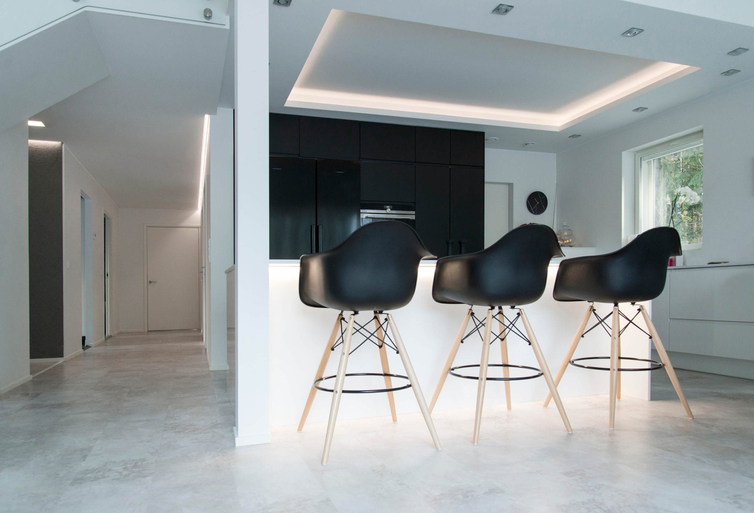 LedStore.fi:n valikoimaan kuuluu LED-valaistus, joka täydentää modernin keittiön minimalista muotoilua. Keittiössä kolmen mustan baarijakkaran puujalat korostavat tyylikkään valkoisen keittiötason ilmettä. Tilaan luo tunnelmaa pehmeä LED-valaistus, ja tummat kaapistot muodostavat elegantin kontrastin vaaleaan lattiaan ja seiniin nähden.