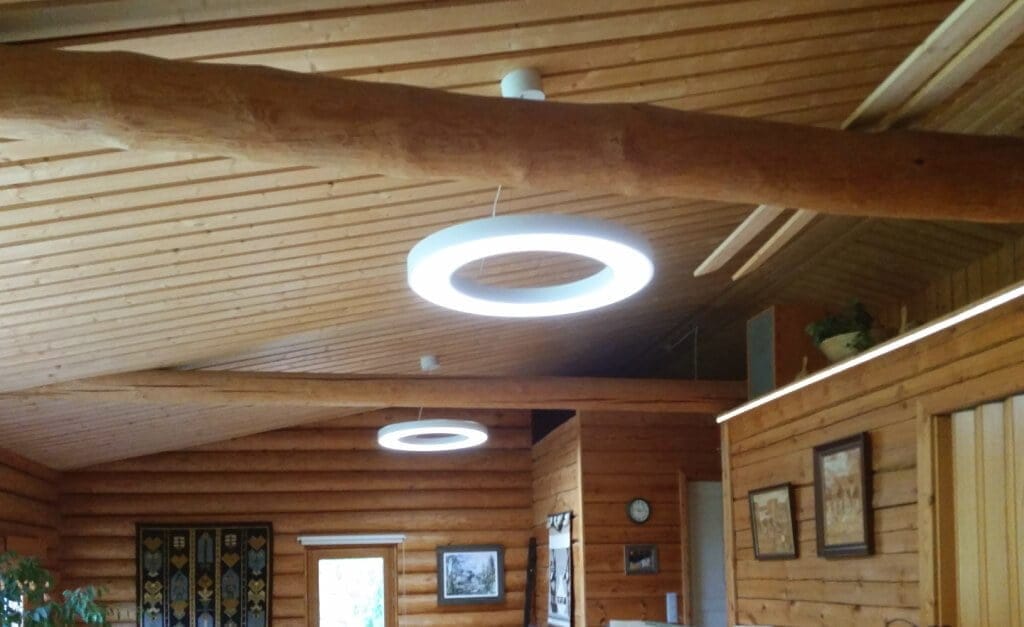 LedStore.fi verkkokaupasta löydät täydelliset led-valaisimet luomaan tunnelmaa rustiikkiseen huoneeseen, jossa på puukatot ja -seinät. Modernt, pyöreät LED-valaisimet tuovat tillaan ajankohtaista tyylikkyyttä. Seiniä koristavat taideteokset ja valokuvat, ja vasemmalla näkyy vehreä kasvi. Kauempana oleva seinä saa lisää ilmettä kauniin seinävaatteen avulla.